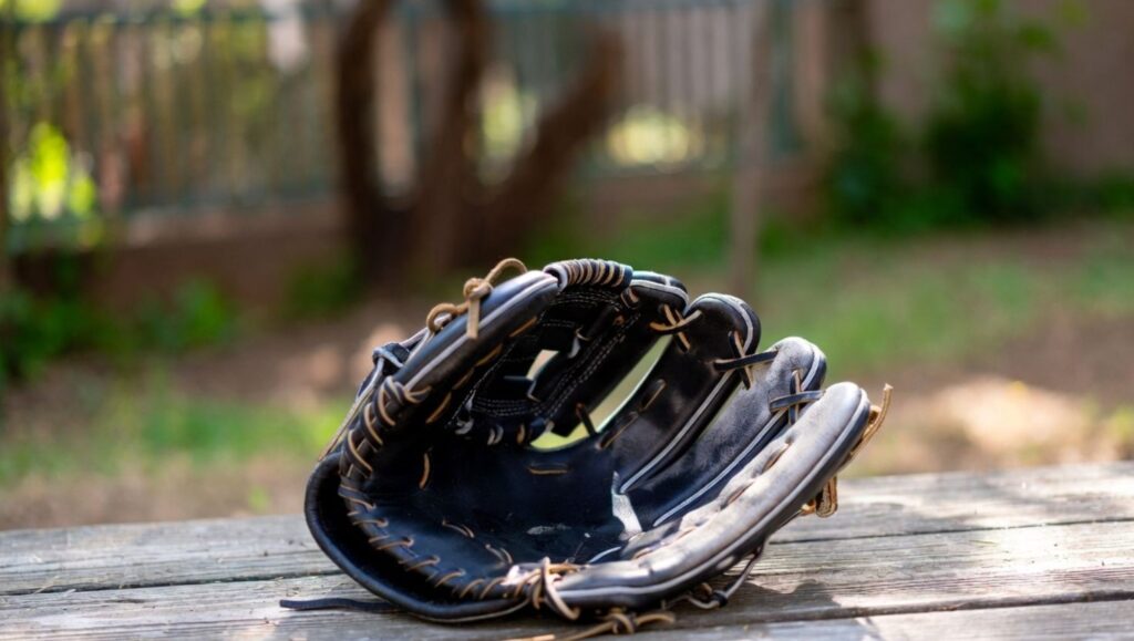 A baseball glove being dried outdoors on a wooden surface