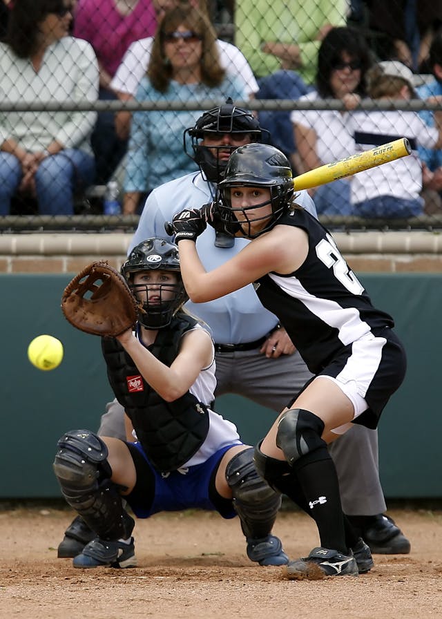 A girl is focusing on baseball ball with a good bat 